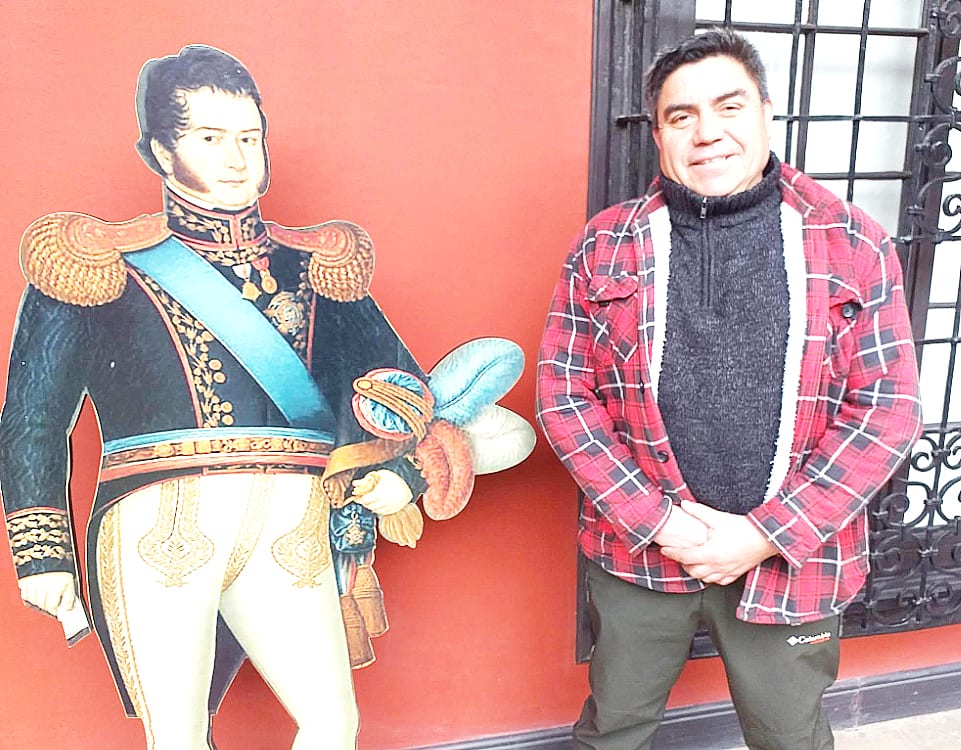 Visitante junto a una figura a tamaño real de Bernardo O’Higgins frente a una pared roja