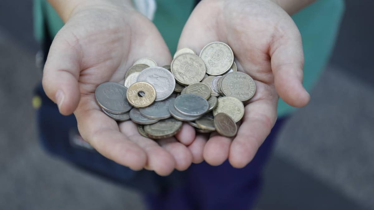 Manos sostienen un puñado de monedas españolas antiguas de distintas épocas y metales, entre ellas pesetas con el escudo de España