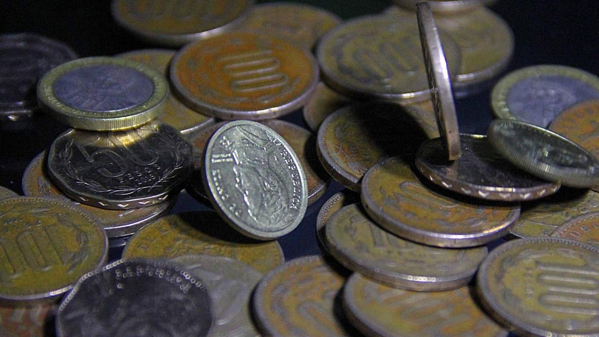 Primer plano de monedas chilenas antiguas apiladas, con brillo metálico sobre fondo oscuro